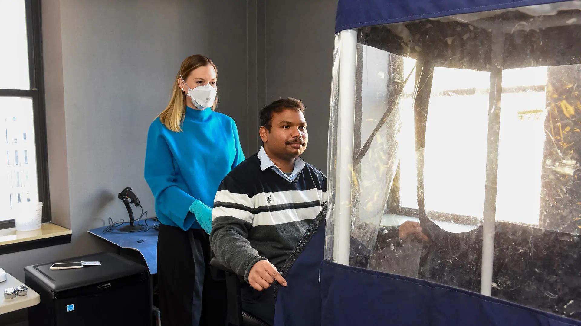 With the help of a Assistant Professor Kristen Coleman of the Maryland Institute for Applied Environmental Health, UMD Faculty Research Associate Aditya Srikakulapu enters a breath sampling station as part of the preparations for a groundbreaking study of flu transmission taking place at a hotel in Baltimore. Photo by Tom Jemski, UMSOM Public Affairs